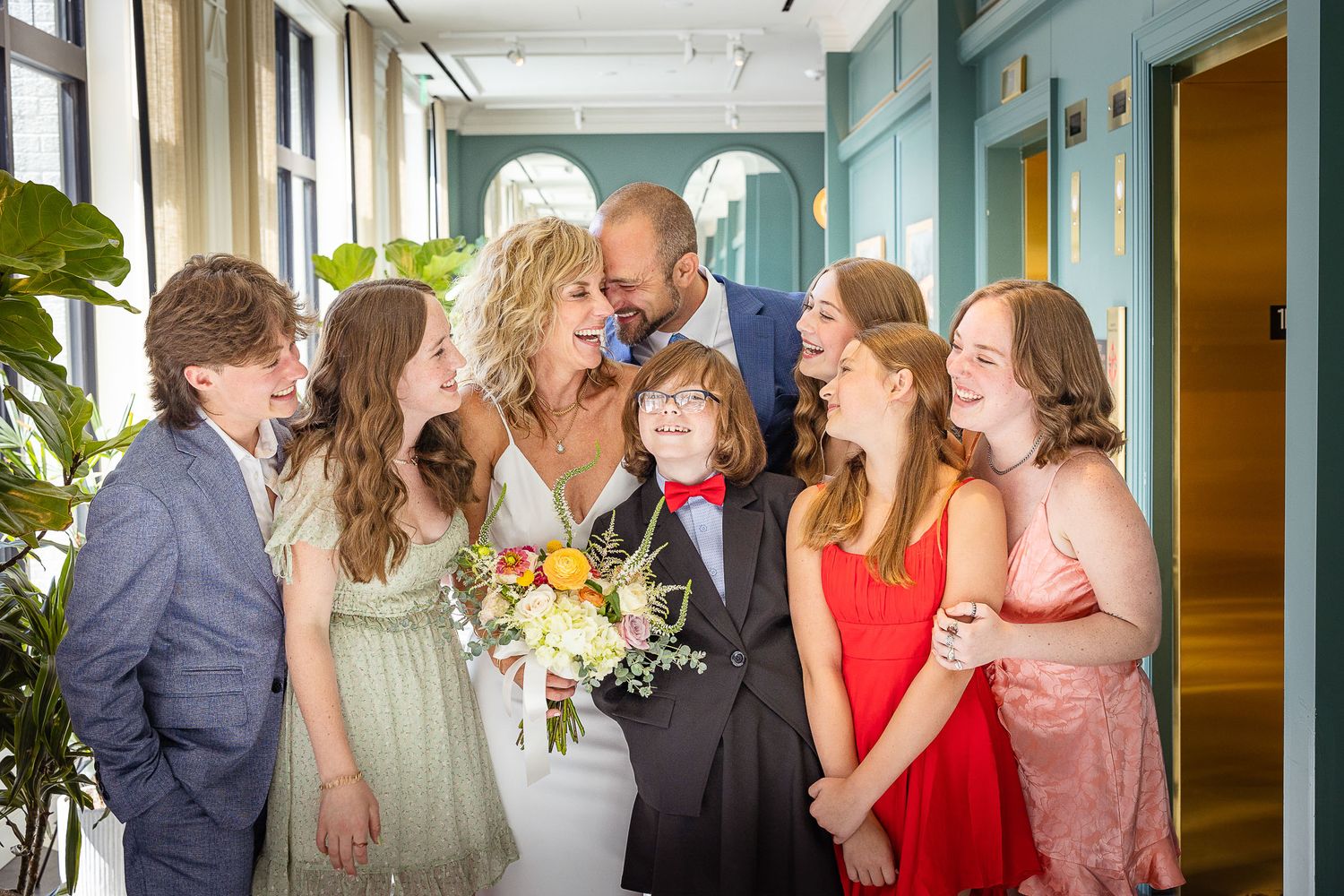 Happy wedding couple kissing surrounded by smiling children in colorful formal attire.