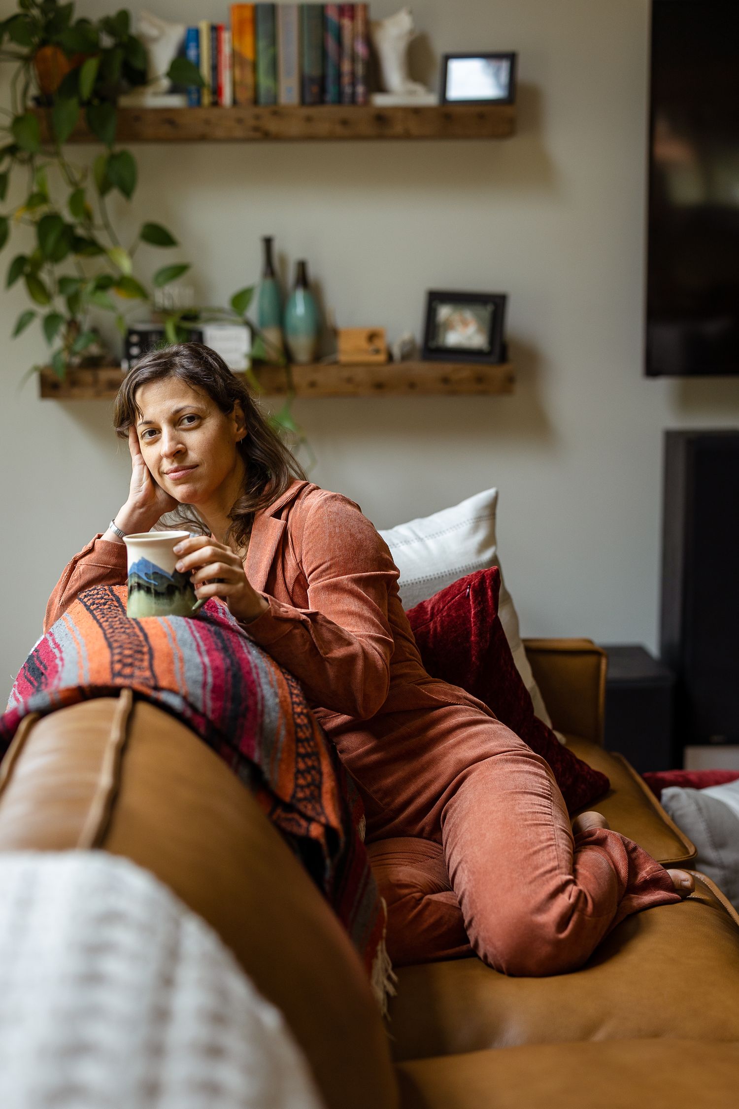 Person relaxing on brown leather couch with colorful pillows in modern living room.