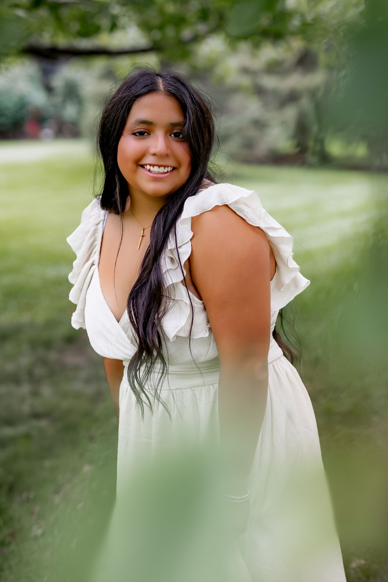 Young woman in white ruffled dress smiling outdoors in lush green garden setting.