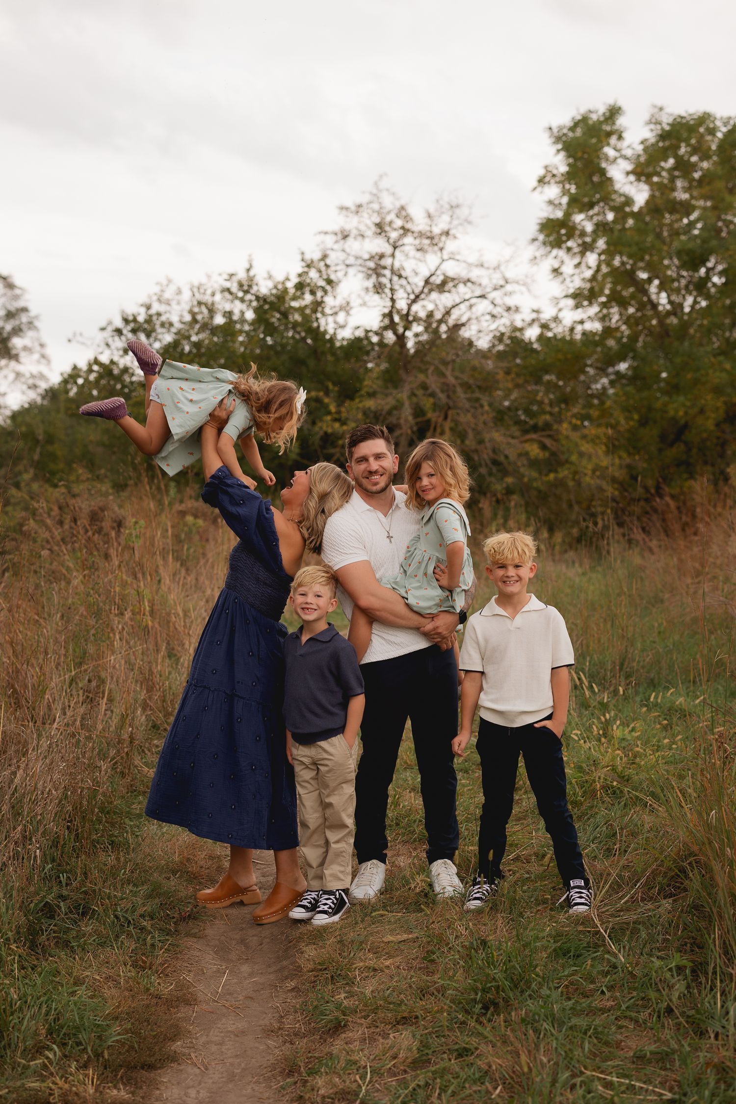 Happy family of six posing together on a nature trail surrounded by lush greenery.