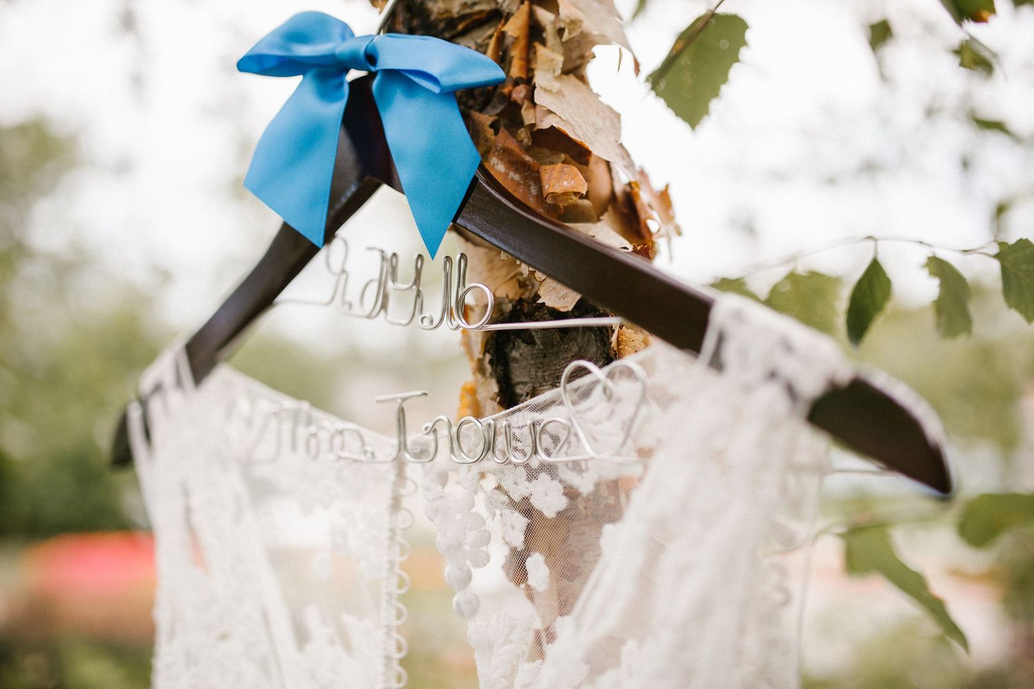 Wedding dress and Mr. & Mrs. hangers with blue bow displayed outdoors on a tree branch.