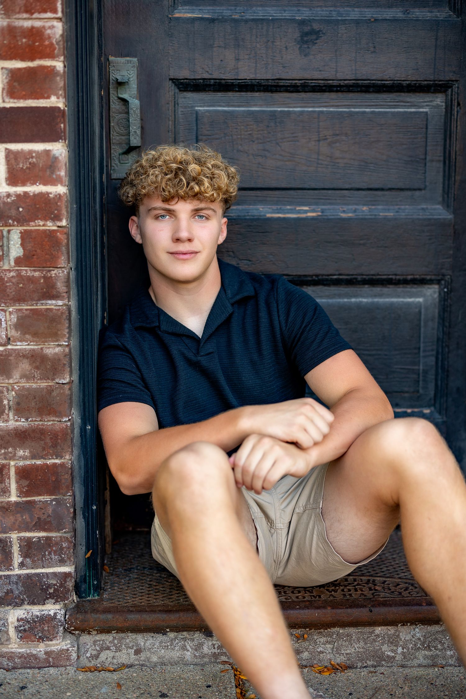 Person sitting on steps against dark wooden door in casual summer attire.