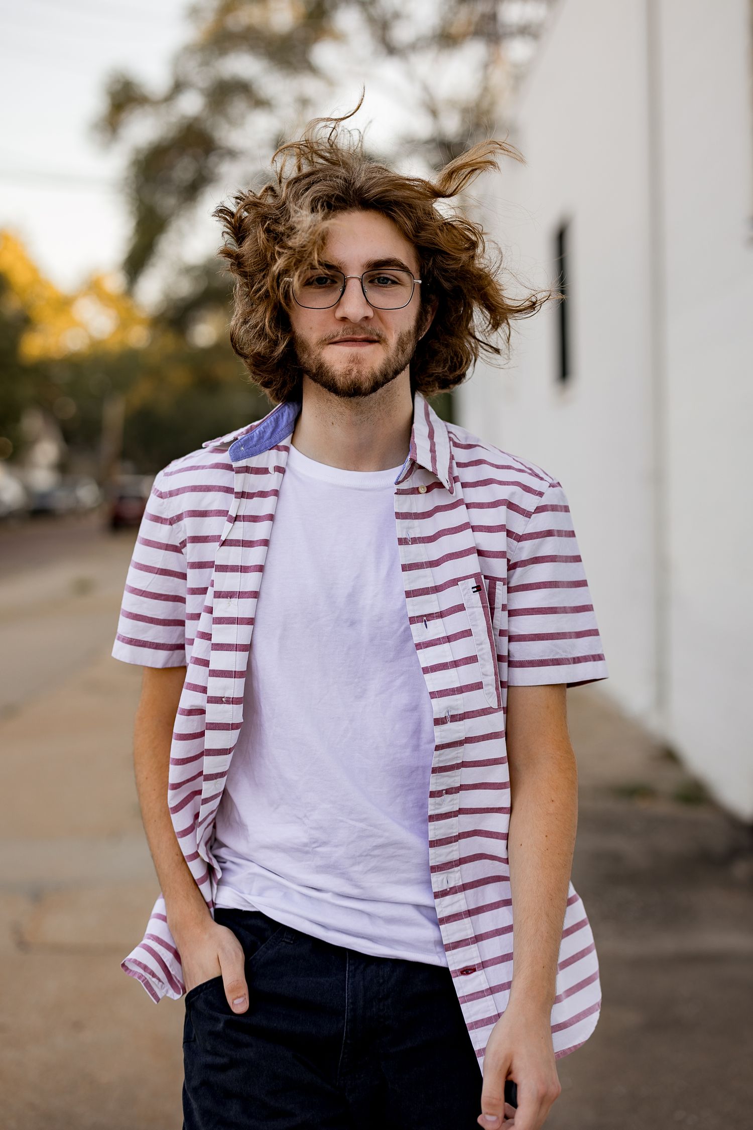 Casual style portrait showing white t-shirt and red striped button-up shirt against an outdoor backdrop.