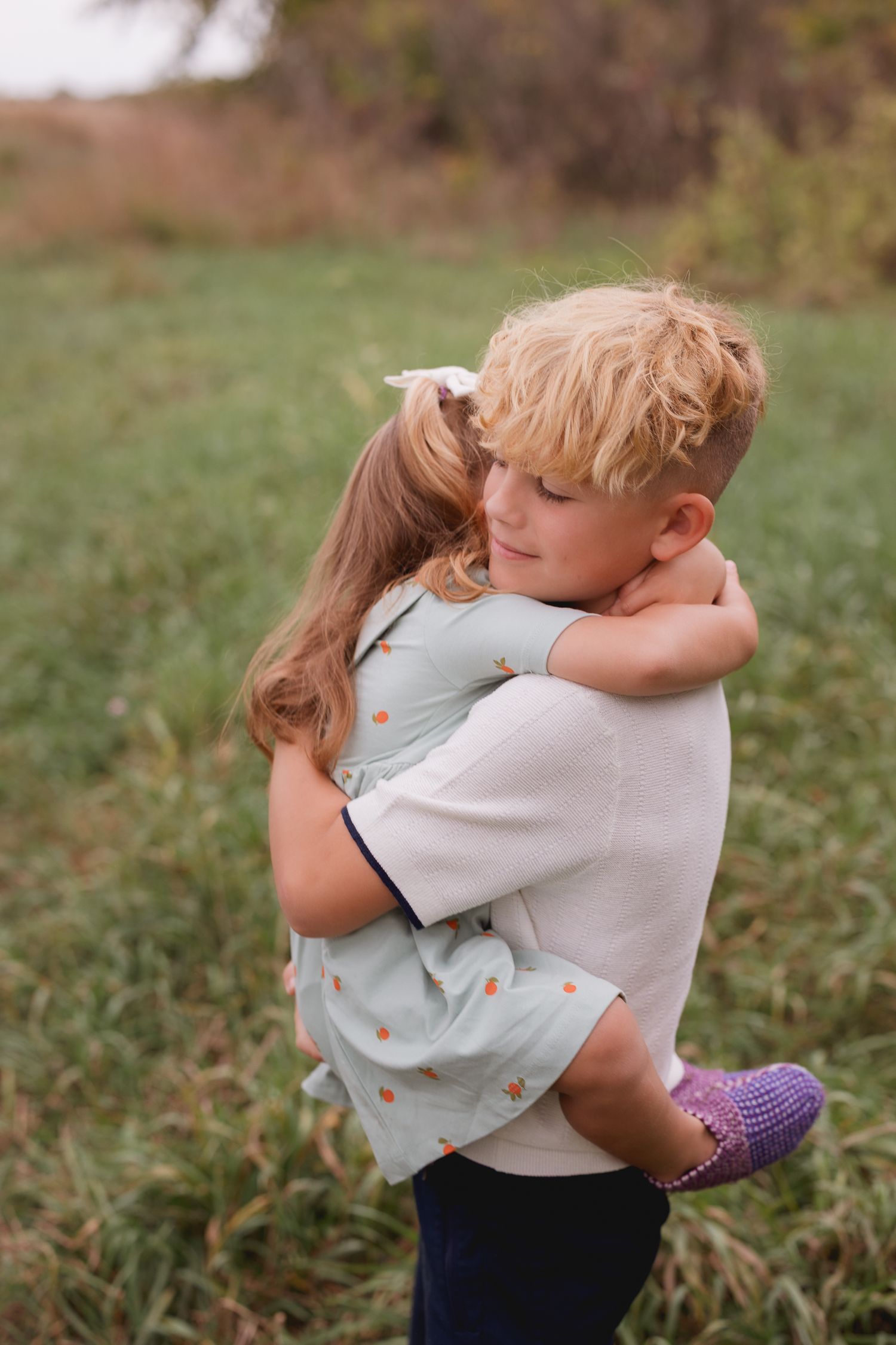 Two young children sharing a warm hug outdoors in a green field, boy holding girl in polka dot dress.