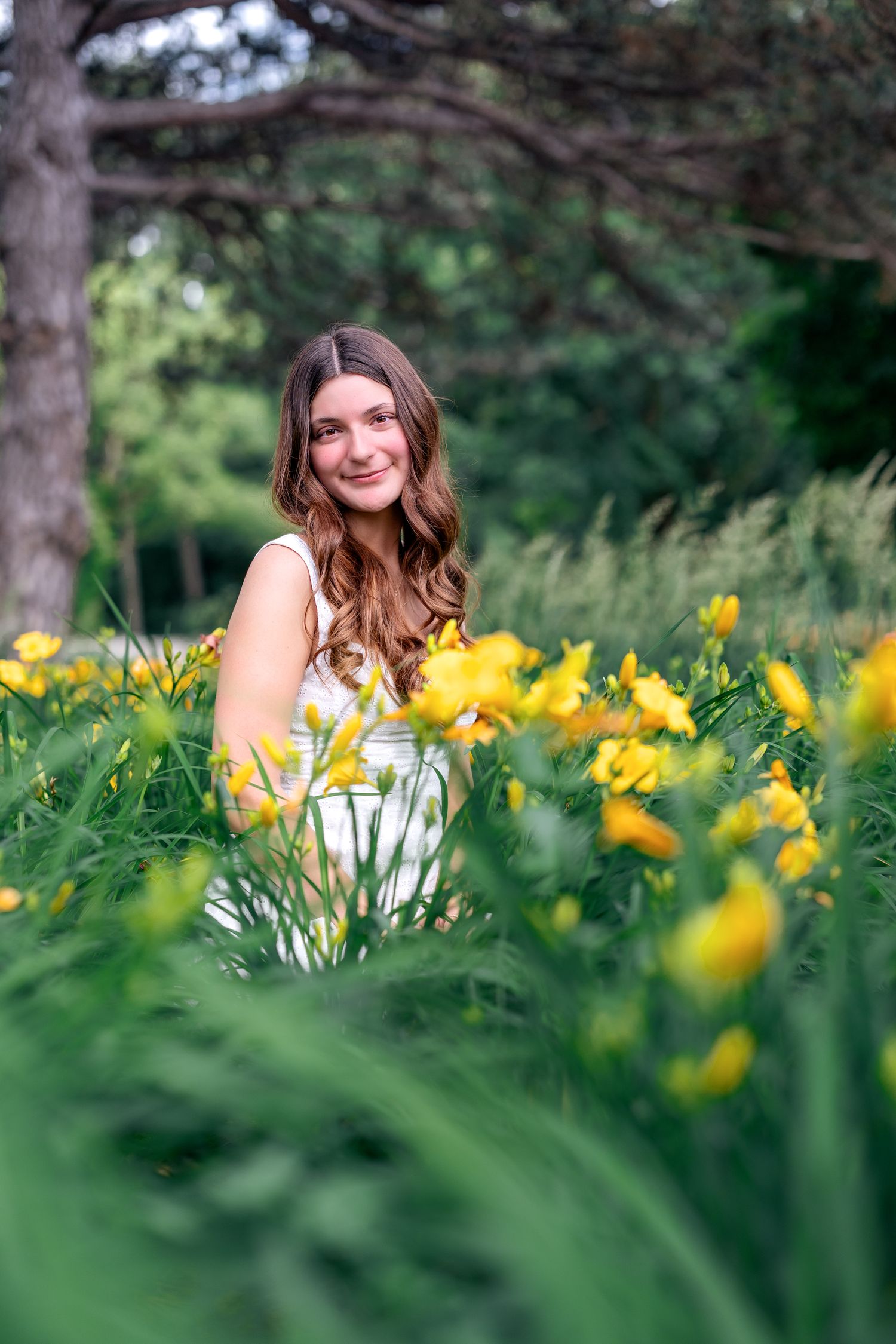 Young woman in white dress smiling among vibrant yellow wildflowers in a lush green garden setting.