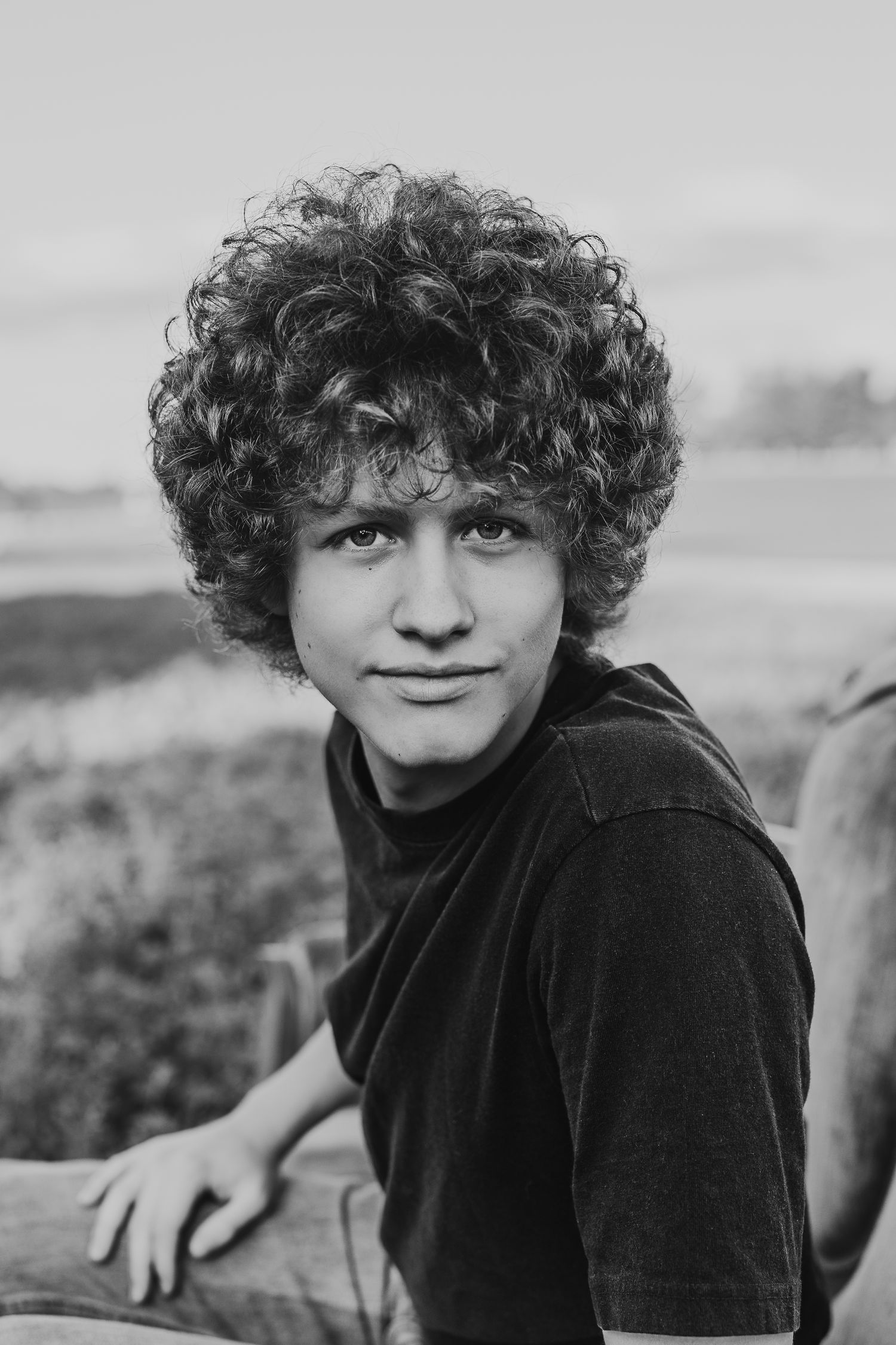 Black and white portrait of a senior with curly hair making expressive faces at the camera.