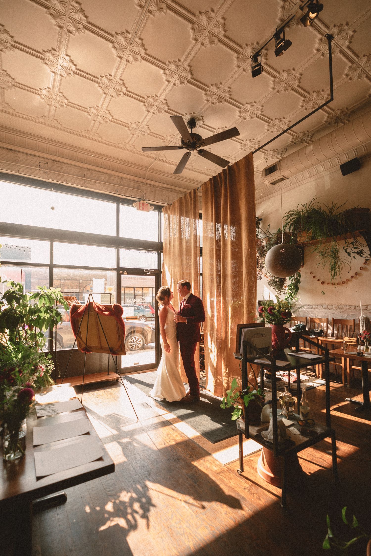 Bride and groom share an intimate moment bathed in golden sunlight inside a charming, plant-filled wedding venue.