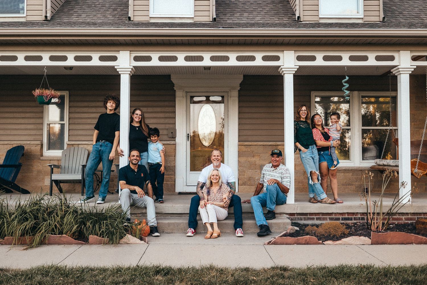 Wide panoramic shot of a family interacting on a house porch with tan siding.