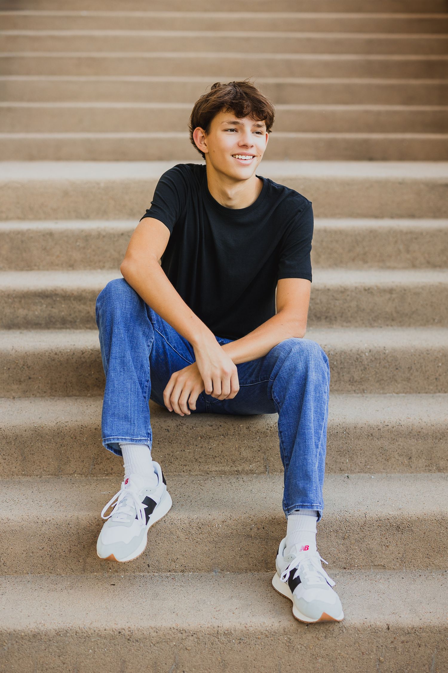 Casual portrait of young person sitting on concrete steps wearing jeans and sneakers.