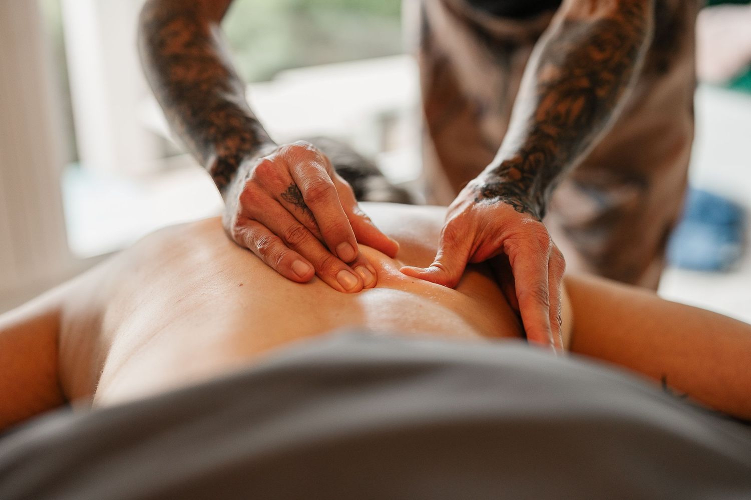 Tattooed therapist performing deep tissue massage on client's back in a professional spa setting.