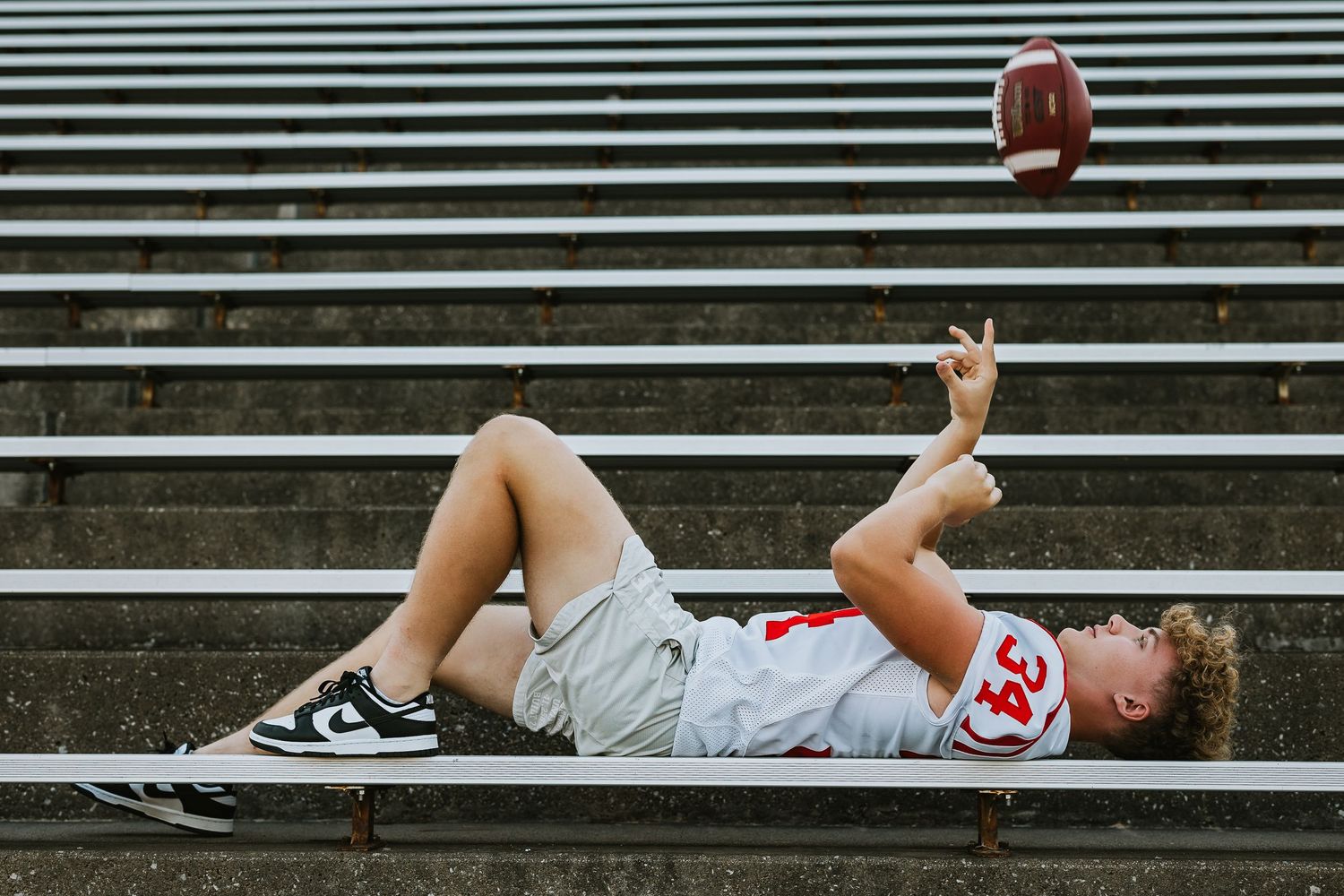 Football plater lying down on bleacher steps in sequential action shots, tossing footballing into the sky and catching it.