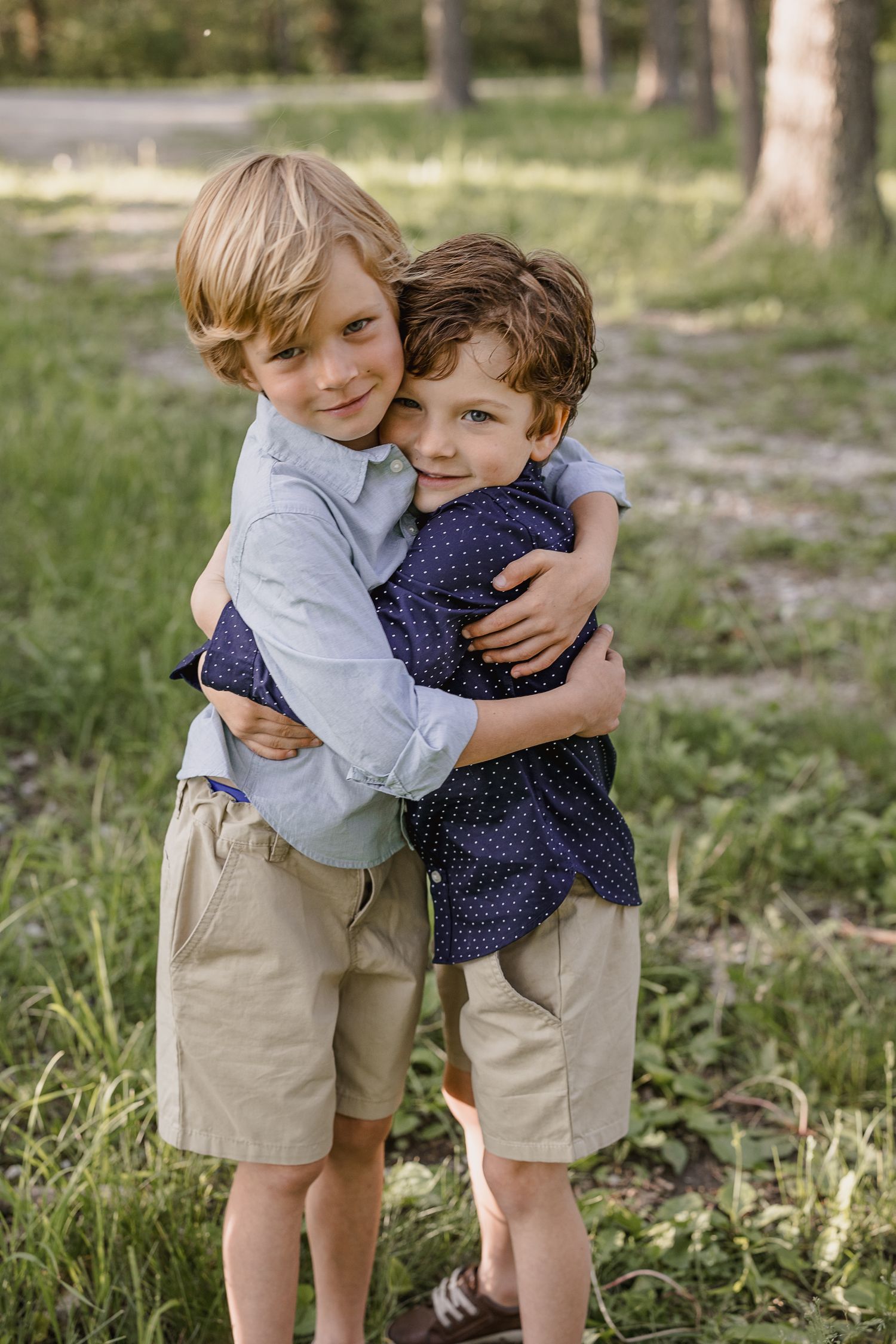 Young siblings share a warm embrace while standing in a sunny outdoor setting.
