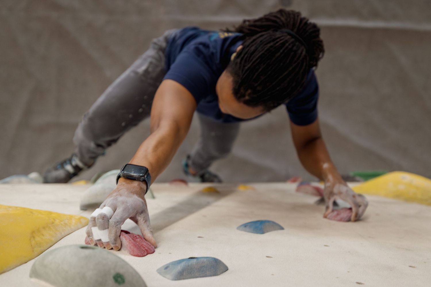 A woman rock climbing on an indoor bouldering wall, gripping colorful holds with chalk-covered hands.