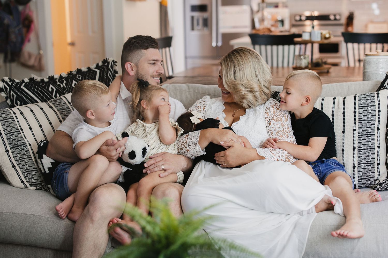 A happy family with two young boys sits together on a cozy striped sofa, sharing a warm and joyful moment at home.