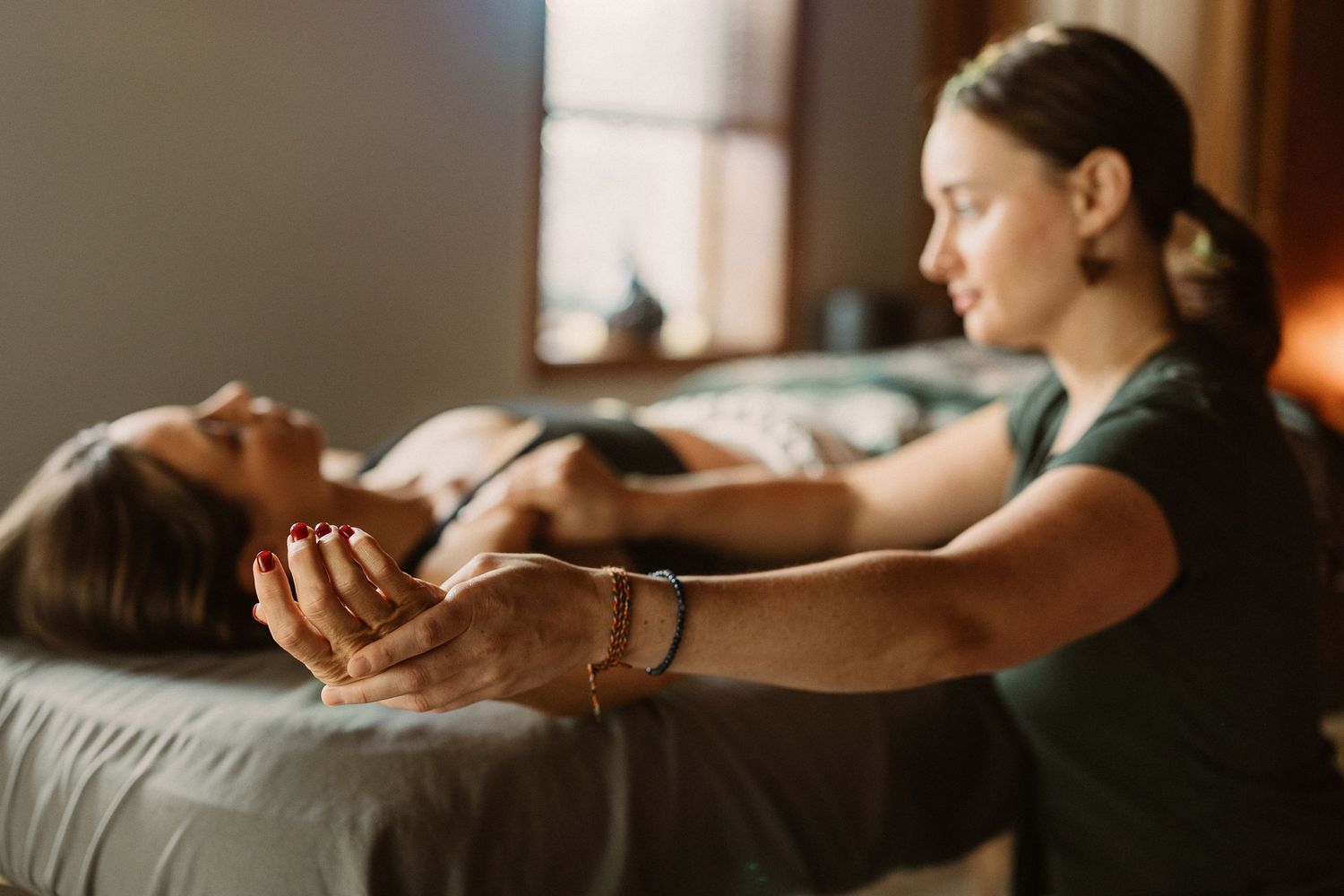 A massage therapist performs a relaxing arm massage on a client lying on a treatment table in a cozy spa room.