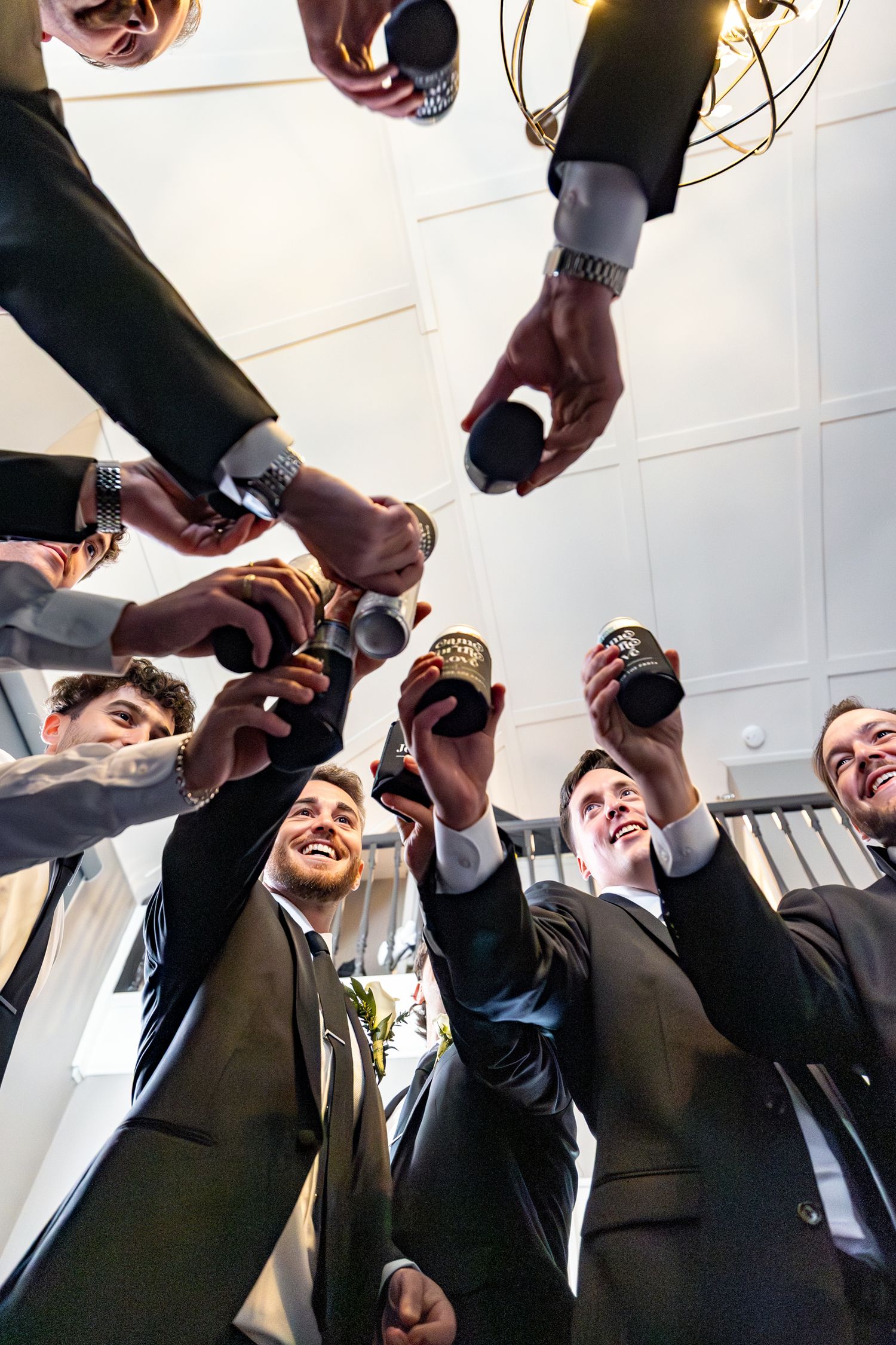 Men in suits toasting with beer bottles in a celebratory circle, viewed from below at a formal event.