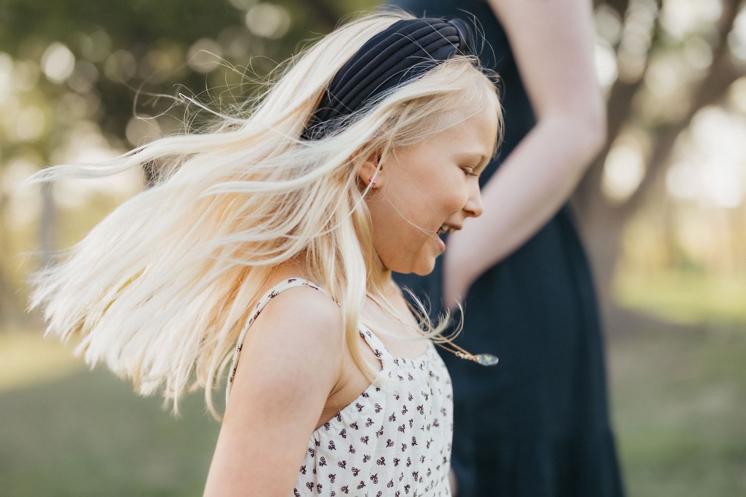 A young blonde girl laughs joyfully as her hair flies in the wind outdoors.