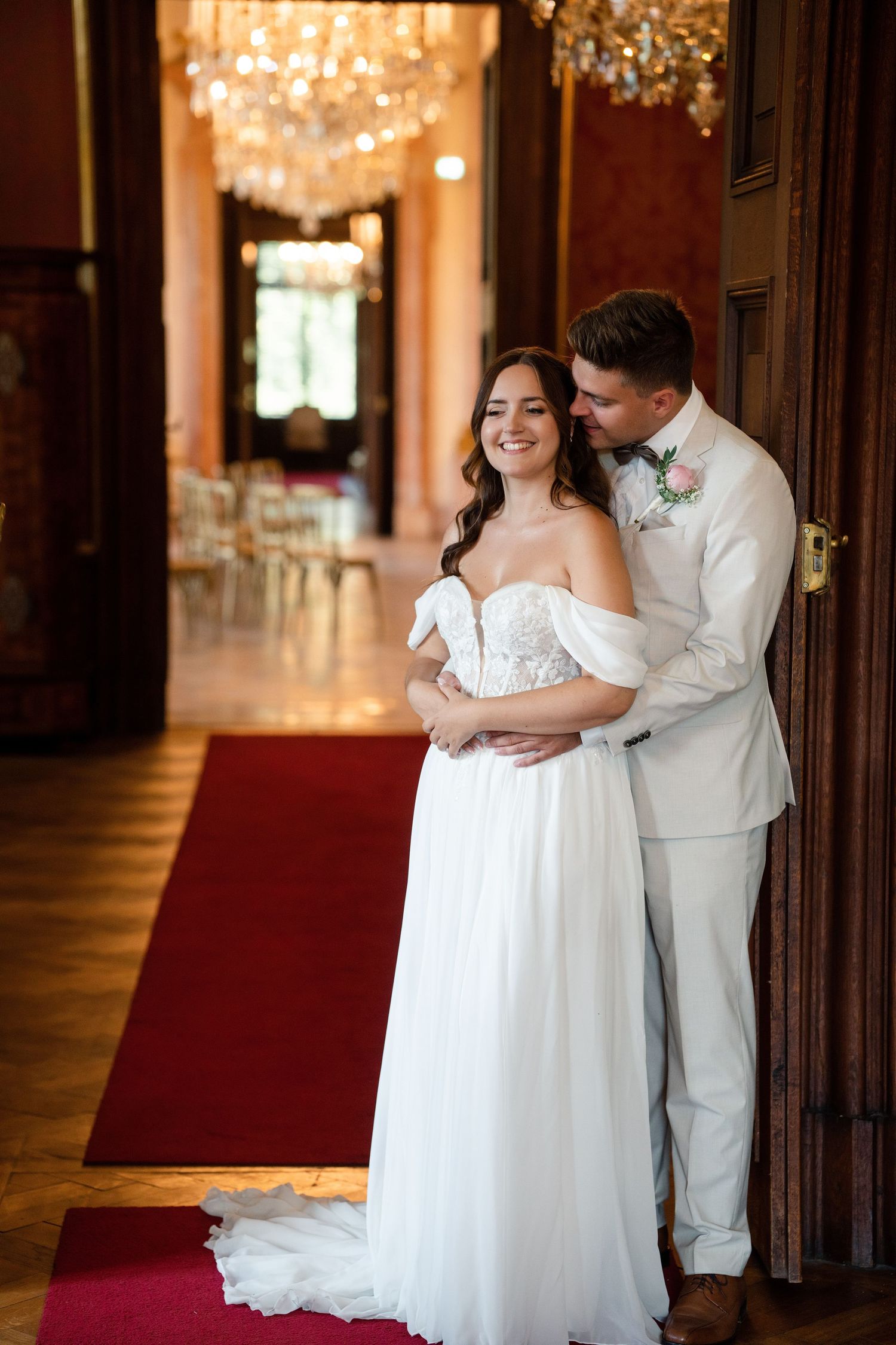 Romantic wedding portrait in luxurious hall with chandelier and red carpet.