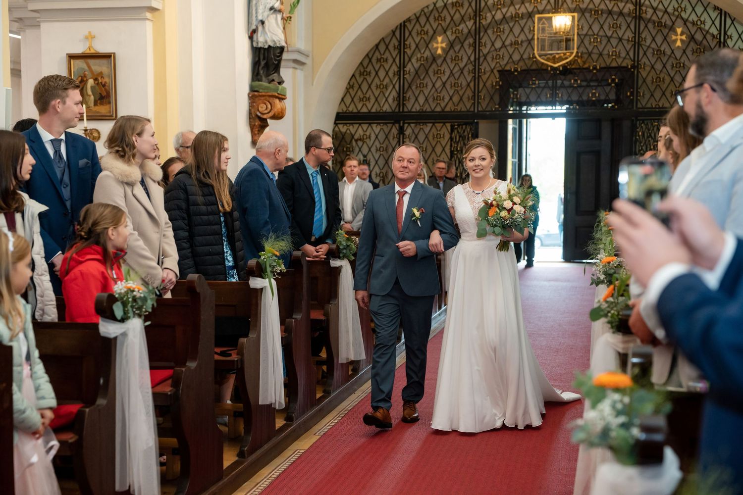 Wedding ceremony guests gather in an elegant church interior with ornate architectural details and warm lighting.