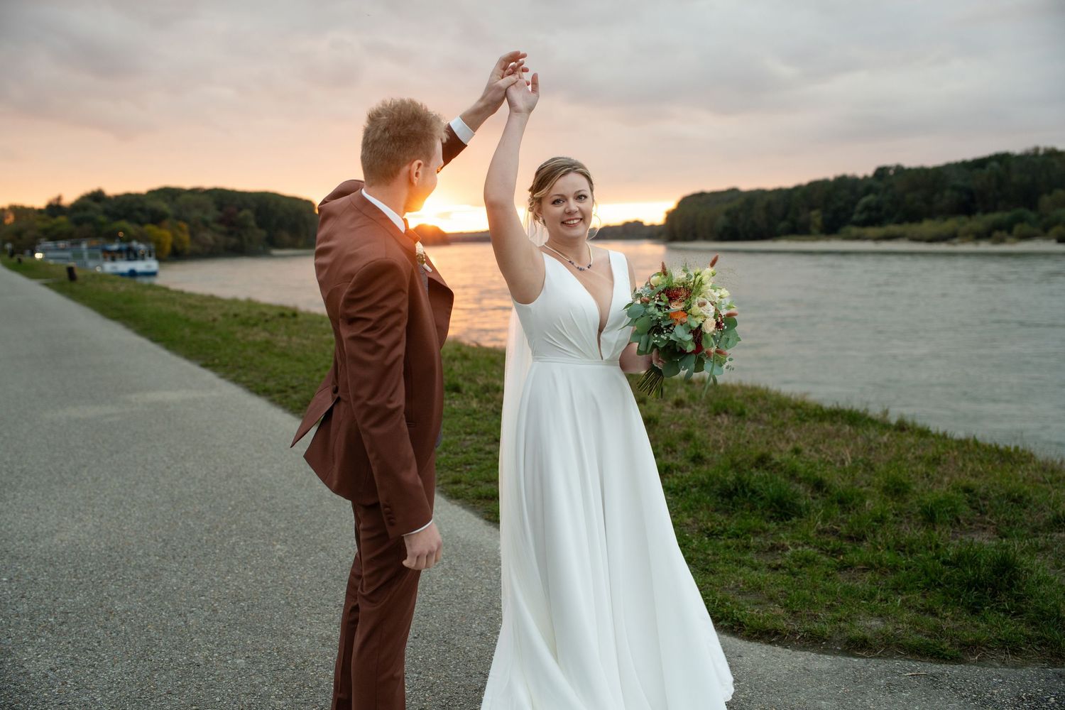 Bride and groom share joyful moment while walking by lake at sunset.