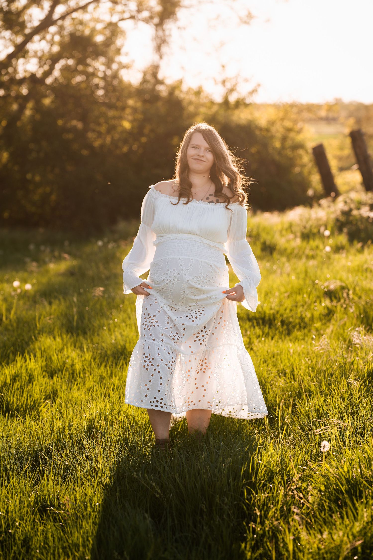 White eyelet dress flowing in golden sunlight on grassy meadow during sunset.