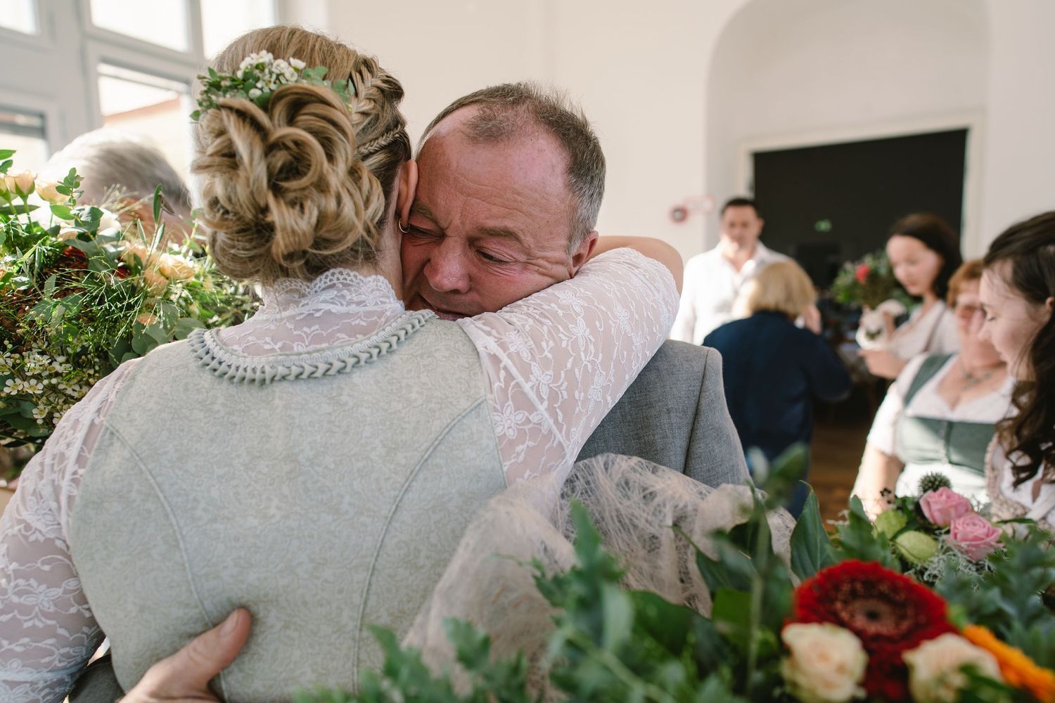A couple shares an intimate embrace during what appears to be a wedding celebration indoors.