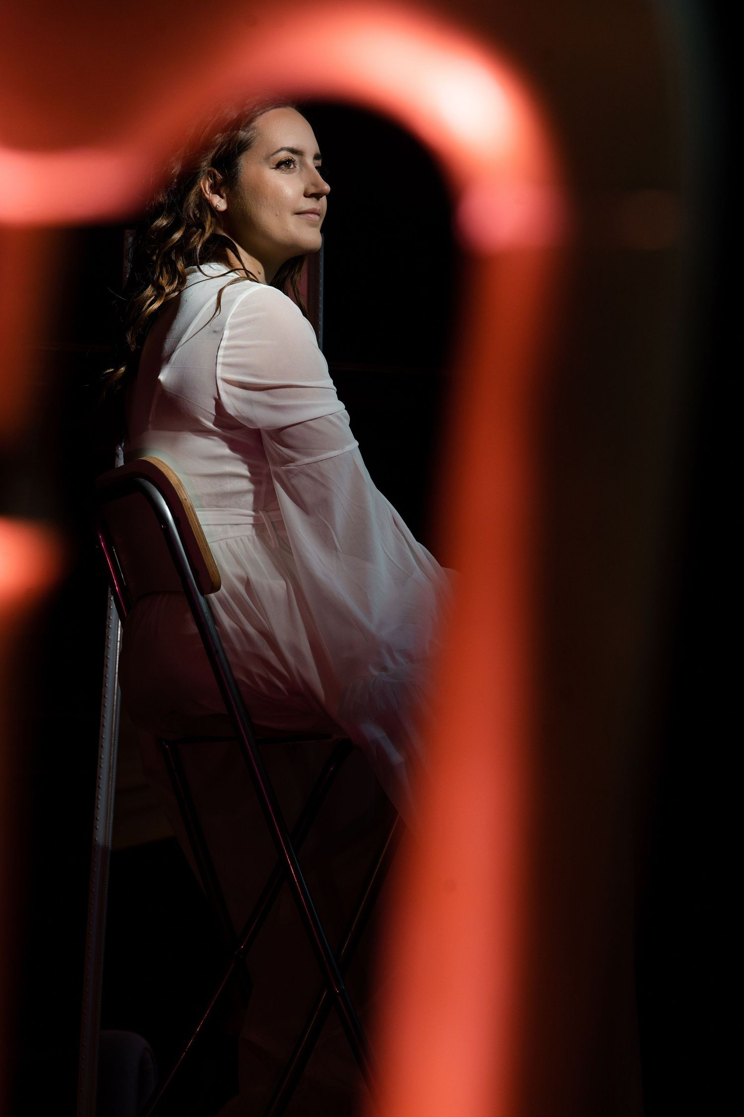 Artistic portrait with dramatic red lighting and white robe against dark background.