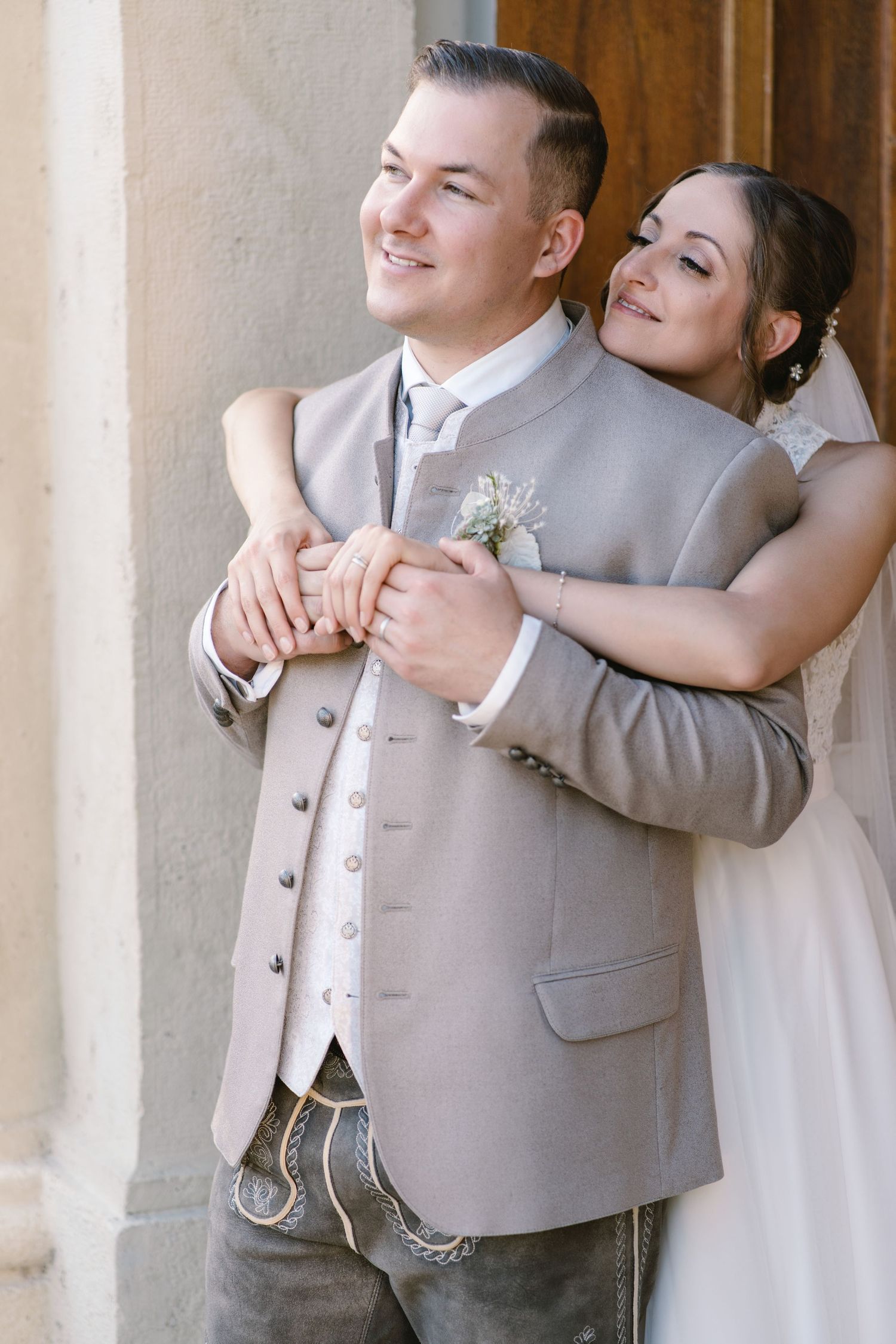 Wedding couple shares playful moment in formal attire against stone columns.