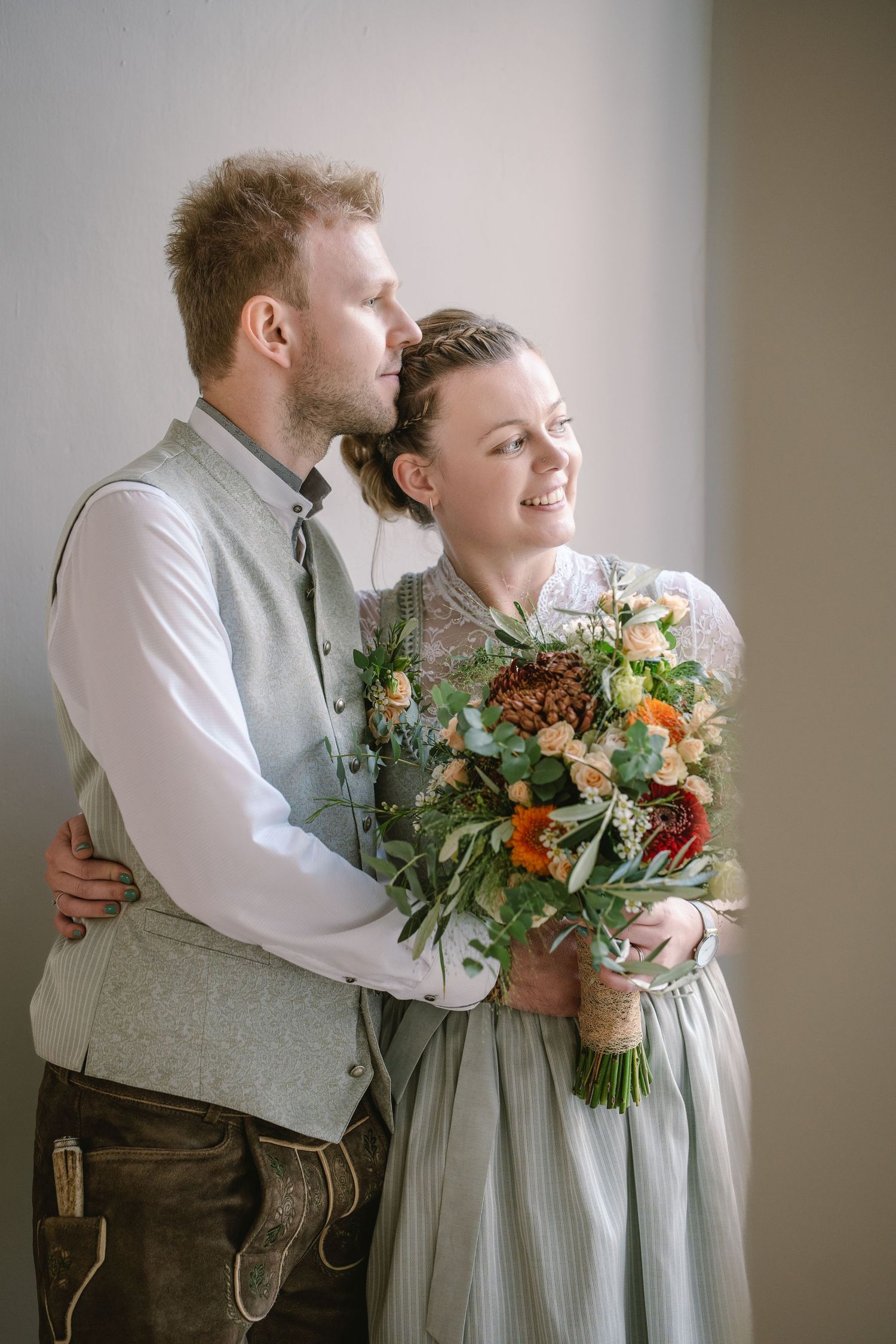 An indoor portrait series showing tender moments between a couple in traditional German dress with a floral bouquet.