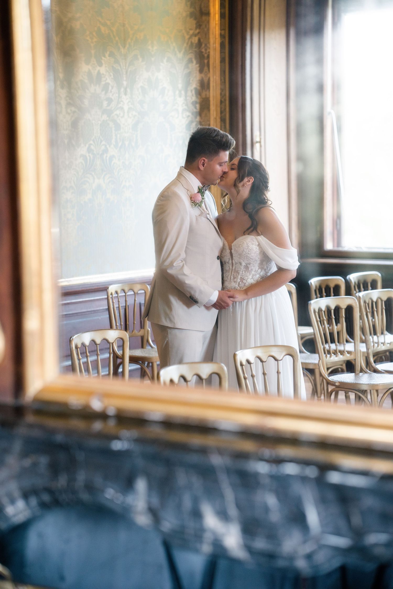 Intimate wedding moment captured through window reflection in grand ballroom setting.