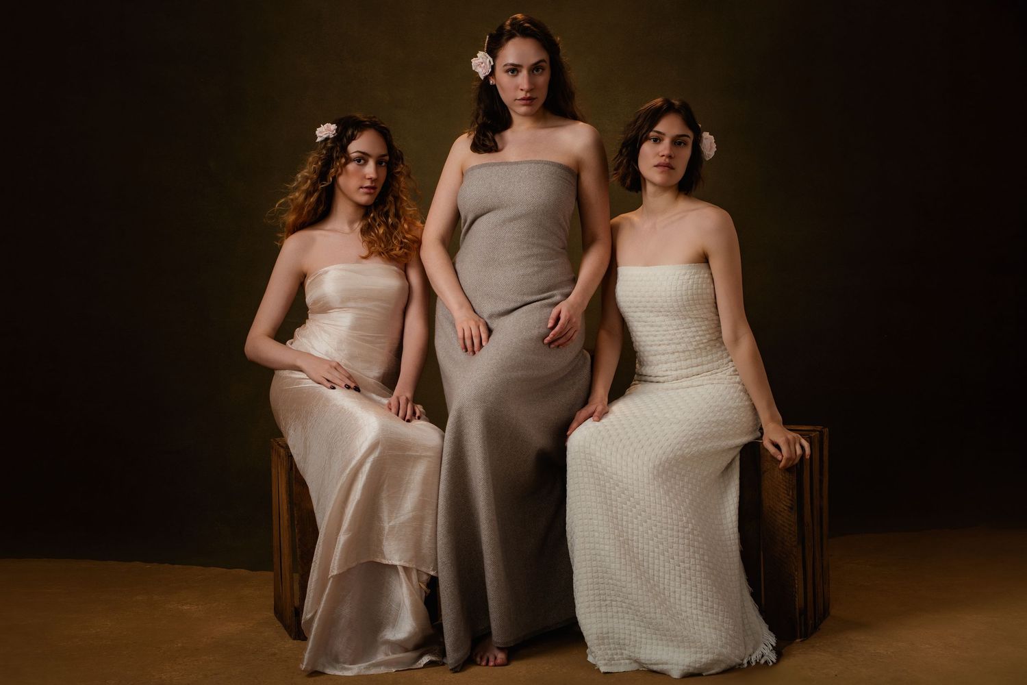 A group of bridesmaids in elegant neutral-toned dresses pose together in a dark studio setting.