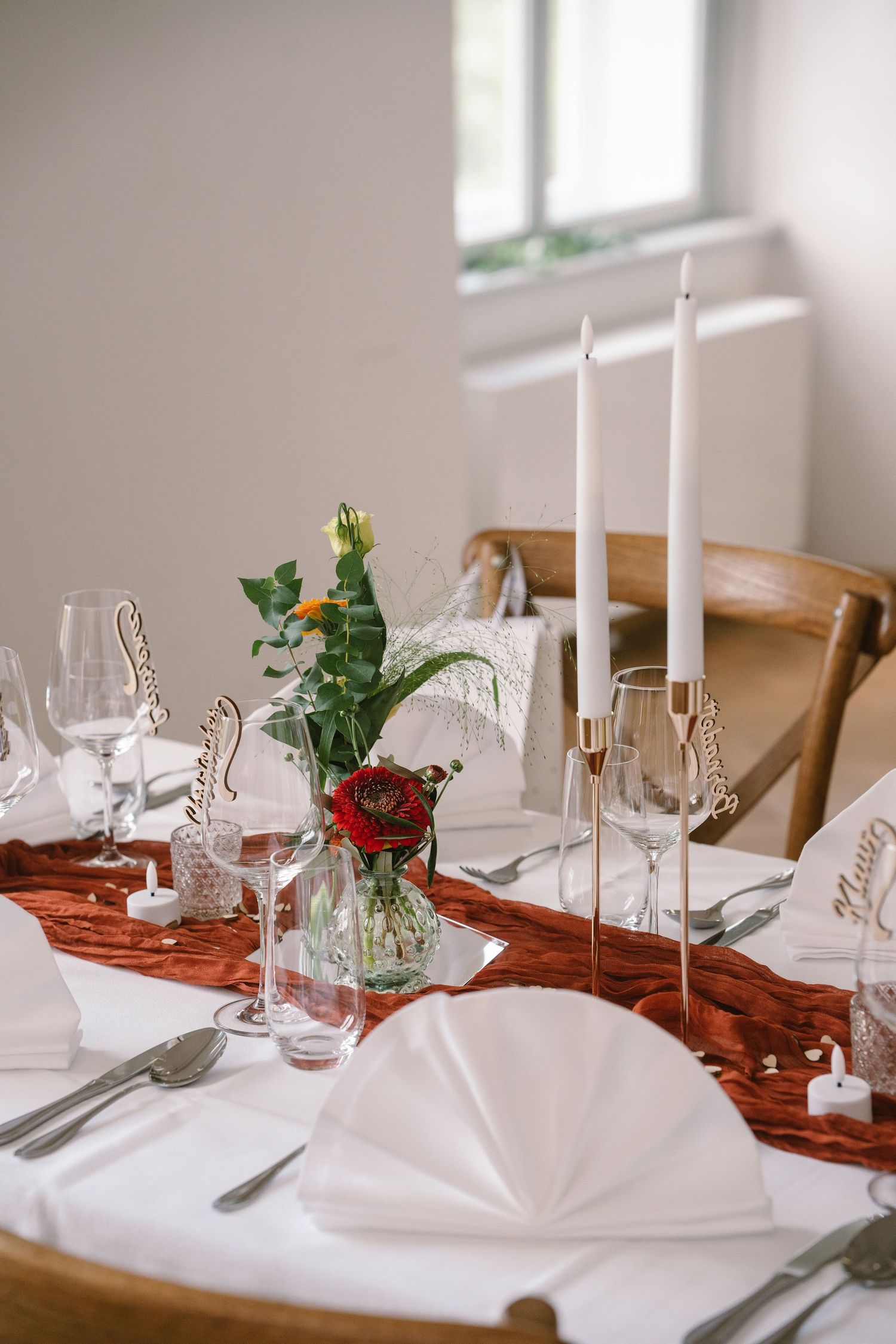 Elegant table setting with white candles, red table runner, folded napkins and wine glasses for formal dining.