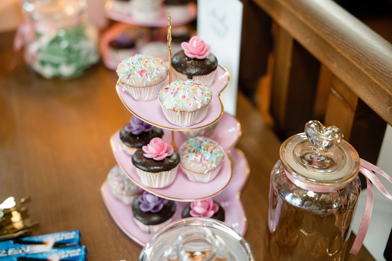 Pink and white decorated dessert stands with floral accents at wedding reception.