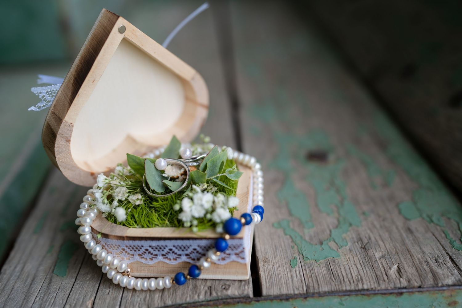 Wedding rings and jewelry details displayed on rustic turquoise wooden surface.