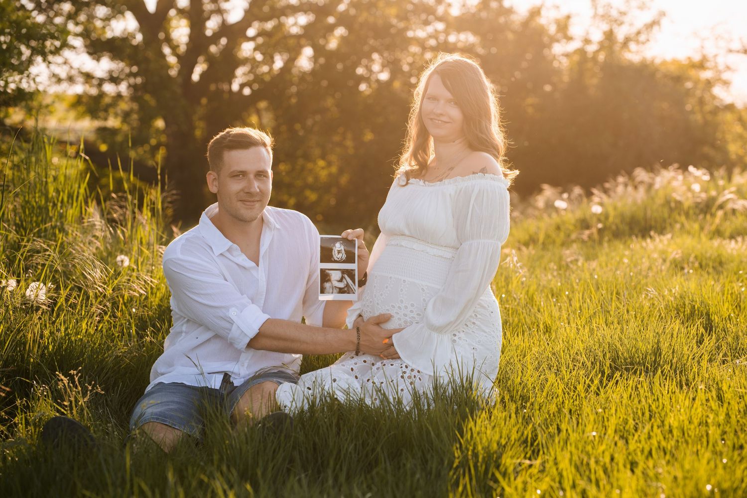 Couple sitting together in golden sunlit meadow during sunset photoshoot.