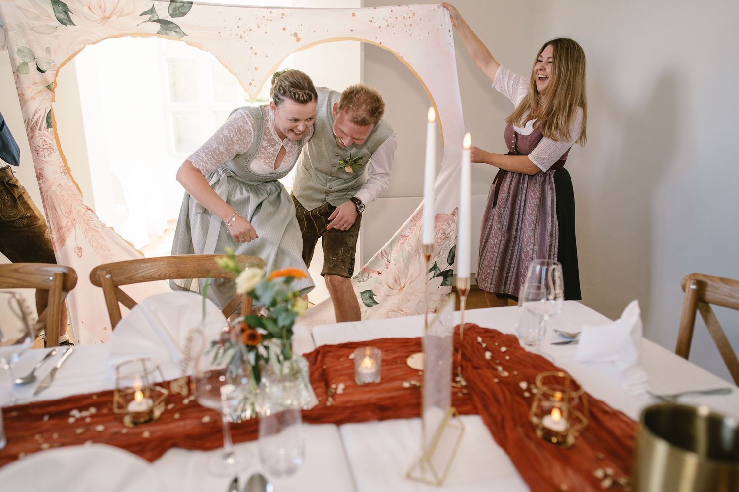 Wedding reception table settings feature rustic decor and floral arrangements in a light-filled space.