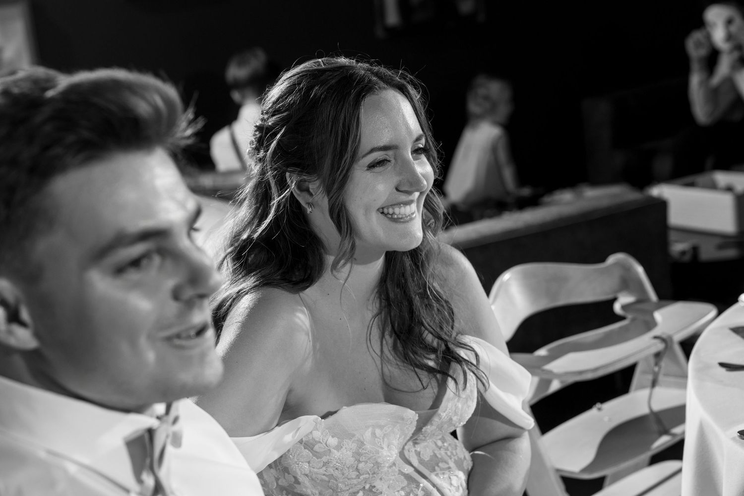 Black and white photo of a smiling bride and groom at their wedding reception table.