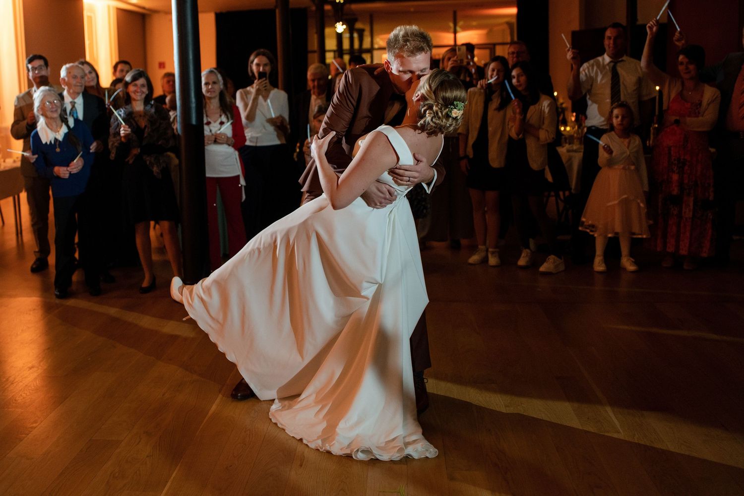 Wedding guests watch a couple dance on a dimly lit ballroom floor.