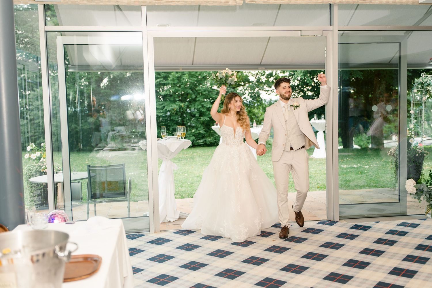 Bride and groom make joyful grand entrance at elegant wedding reception with checkered floor.