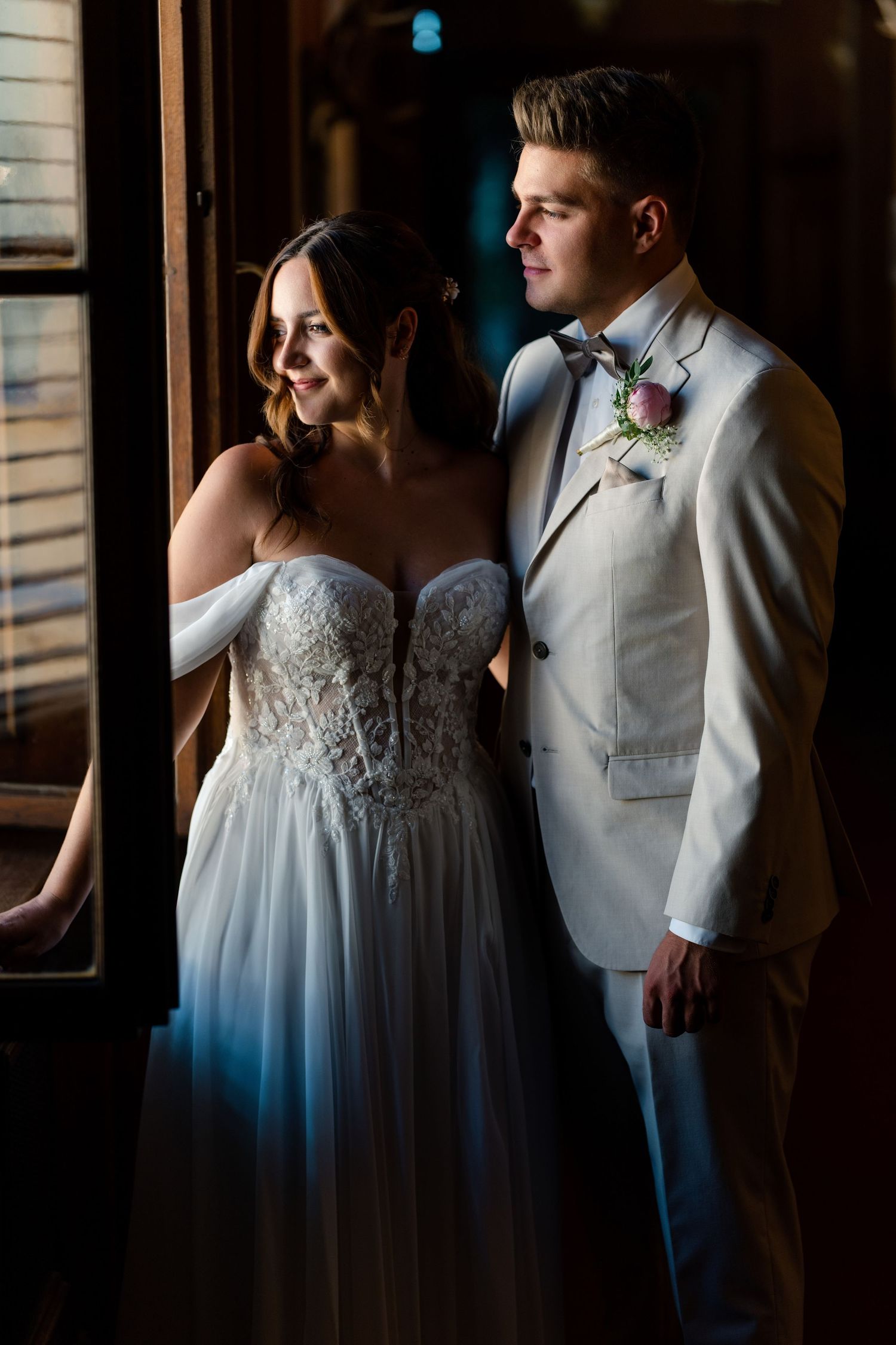A romantic wedding moment captured in moody lighting showing a couple in white attire embracing.
