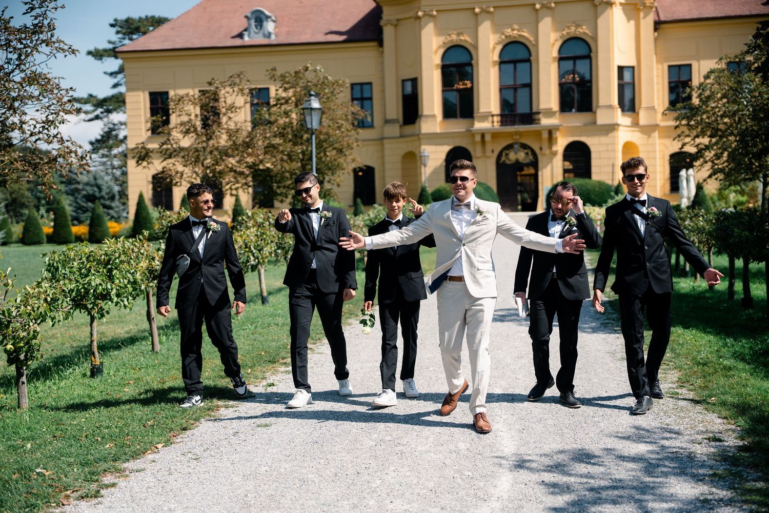 Wedding party poses in front of elegant historic building with arched architecture.