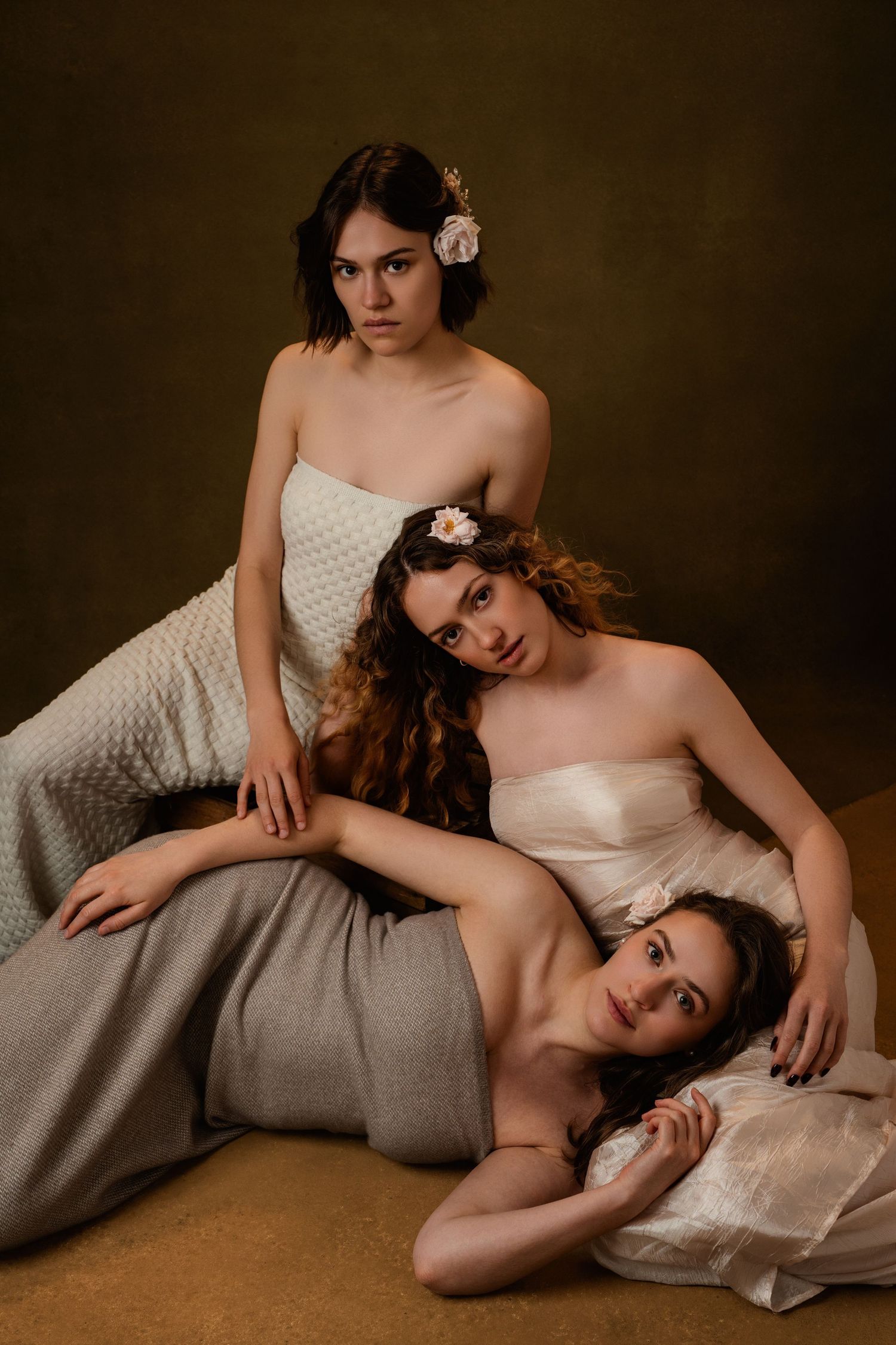 Artistic portrait series showing figure in white dress reclining on gray fabric with moody brown backdrop.