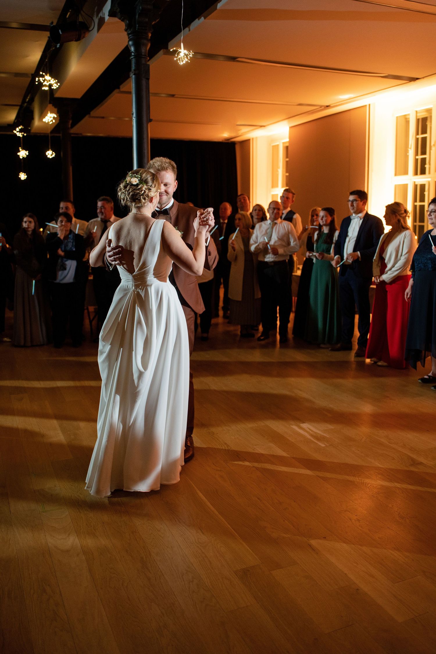 Couples dance on a polished wooden floor during an evening wedding reception in a warmly lit venue.