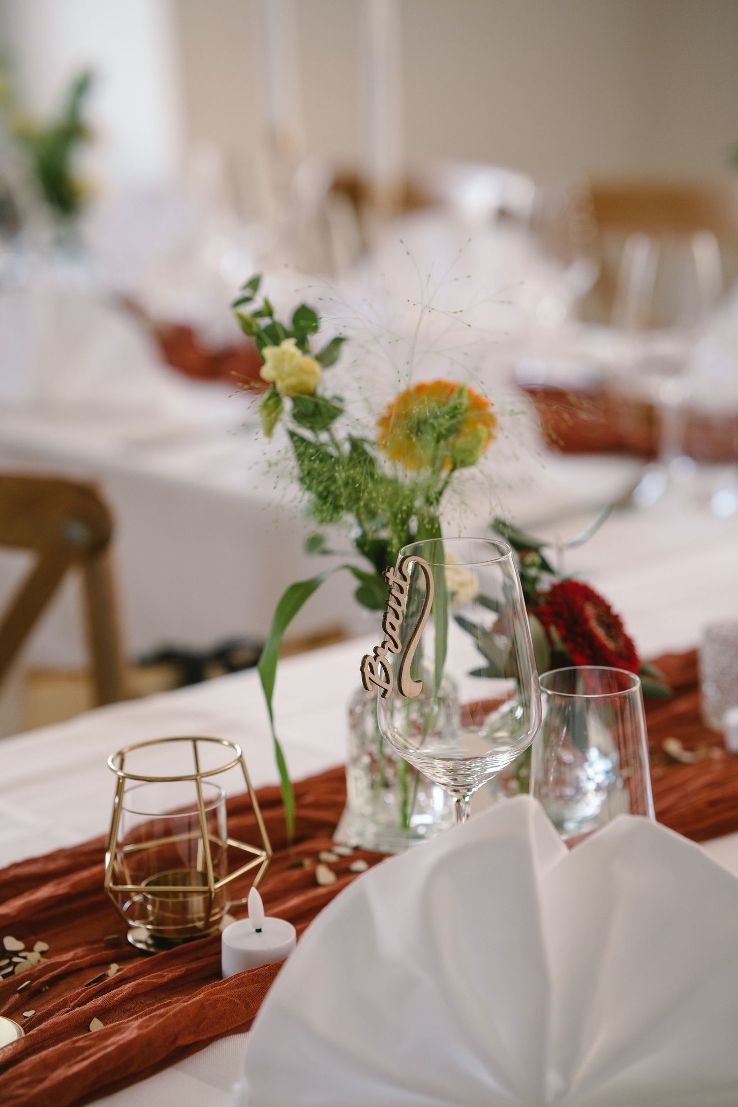Elegant table settings with wine glasses and small floral arrangements on a burgundy table runner.