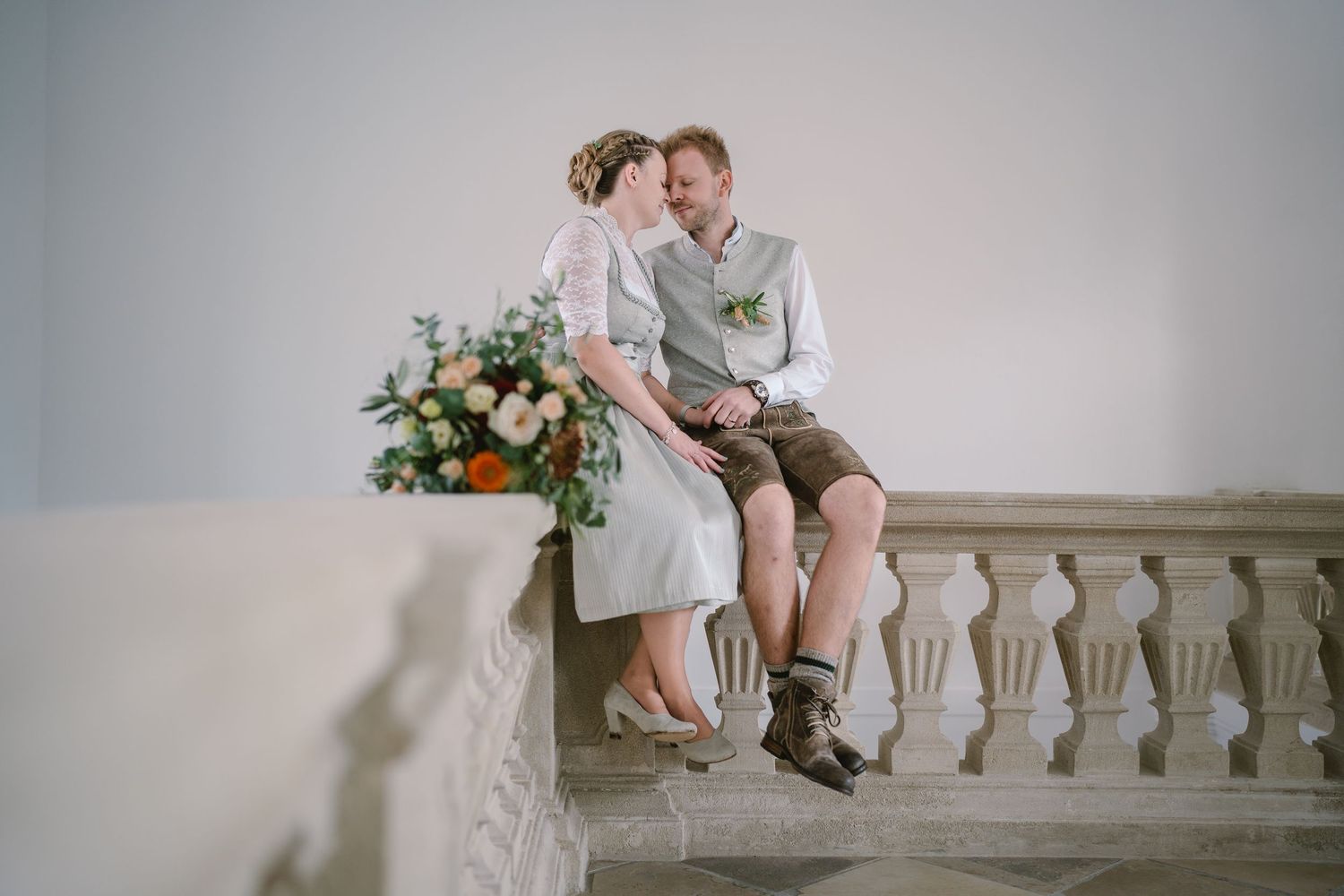 Romantic wedding couple embraces on an elegant stone balcony overlooking a scenic view at sunset.