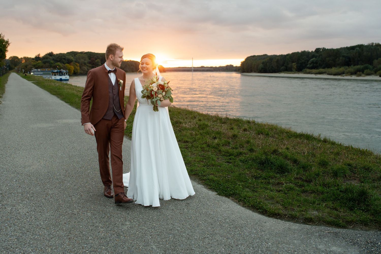 A couple walks along a waterfront path at sunset with dramatic lighting.