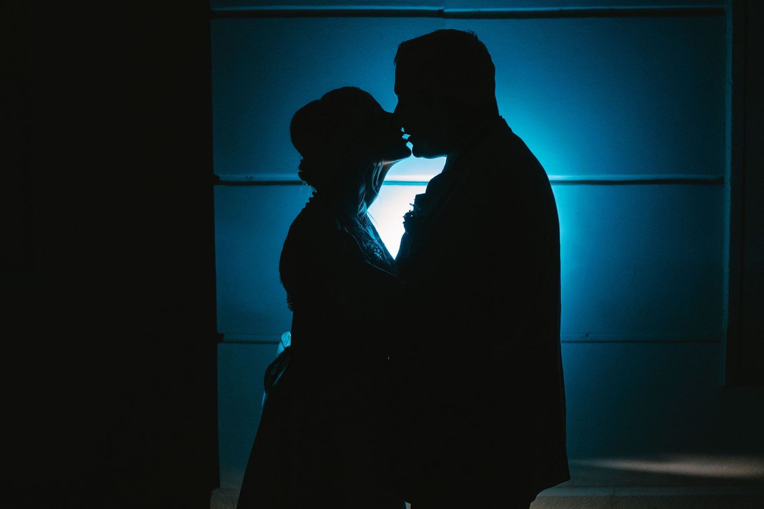 Romantic silhouettes against deep blue backlit background create intimate mood.