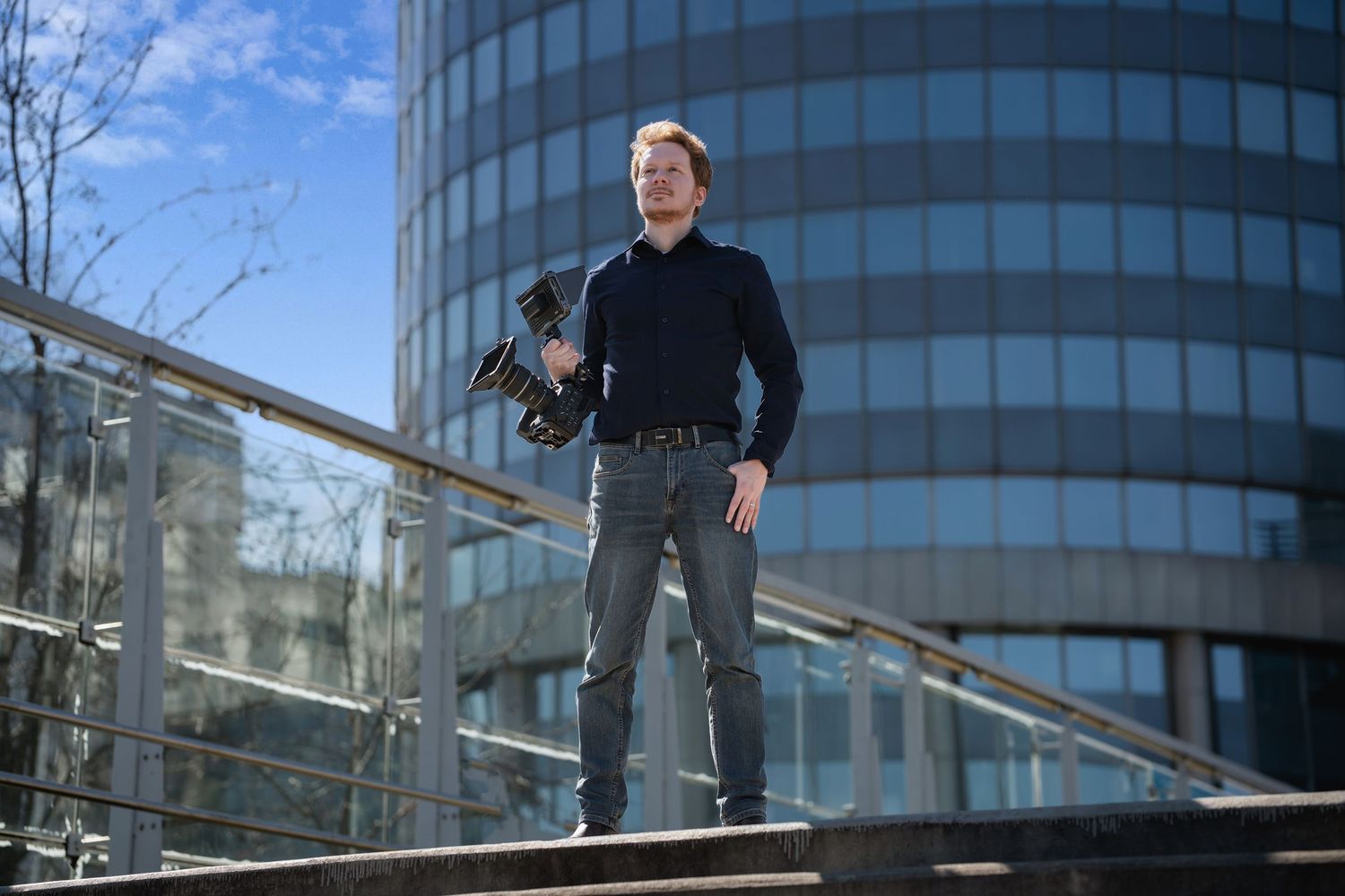 Person in dark clothing walks down modern glass staircase with curved architecture and reflective surfaces.