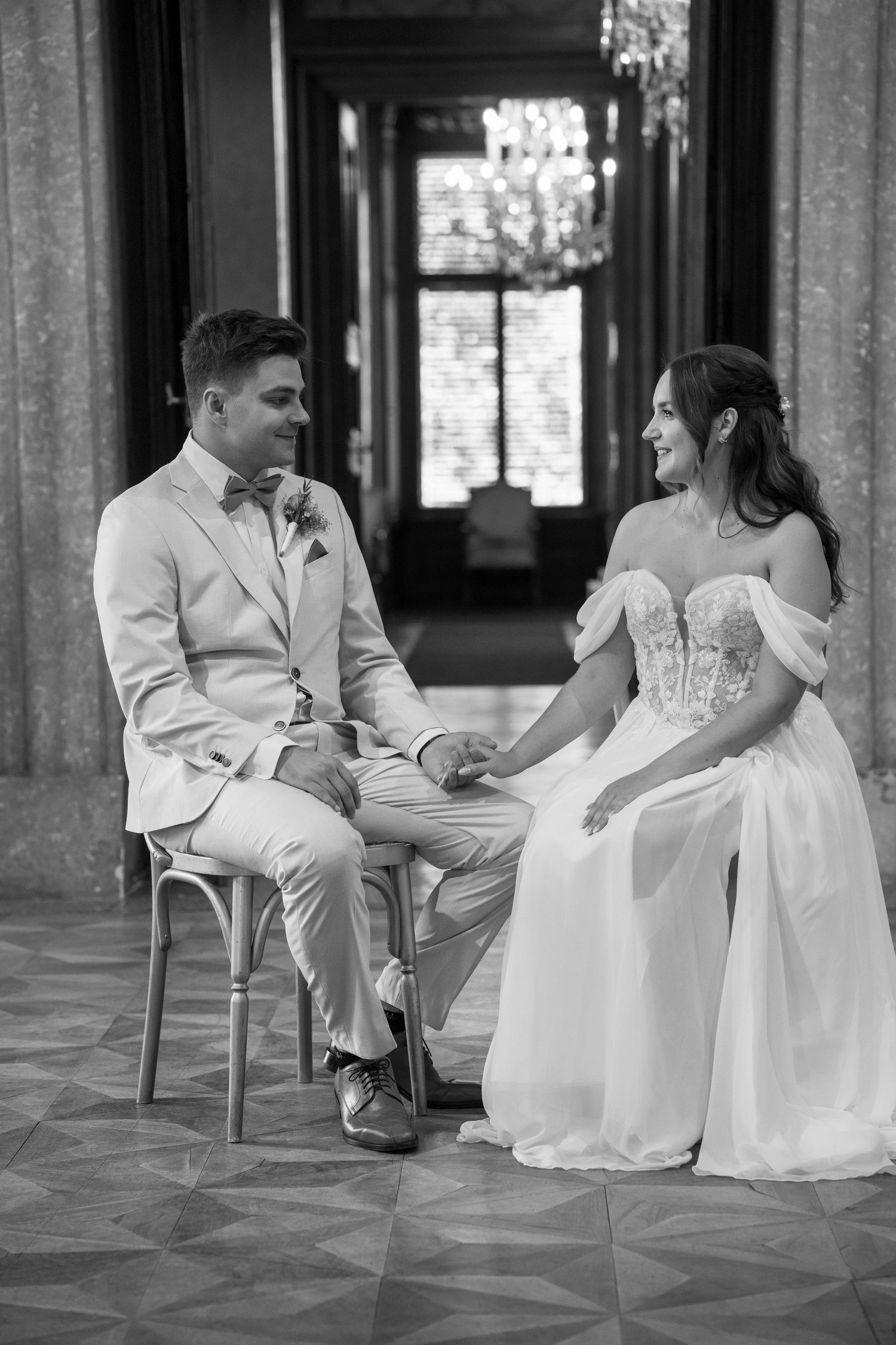 A black and white wedding photo of a couple seated in an elegant hallway.