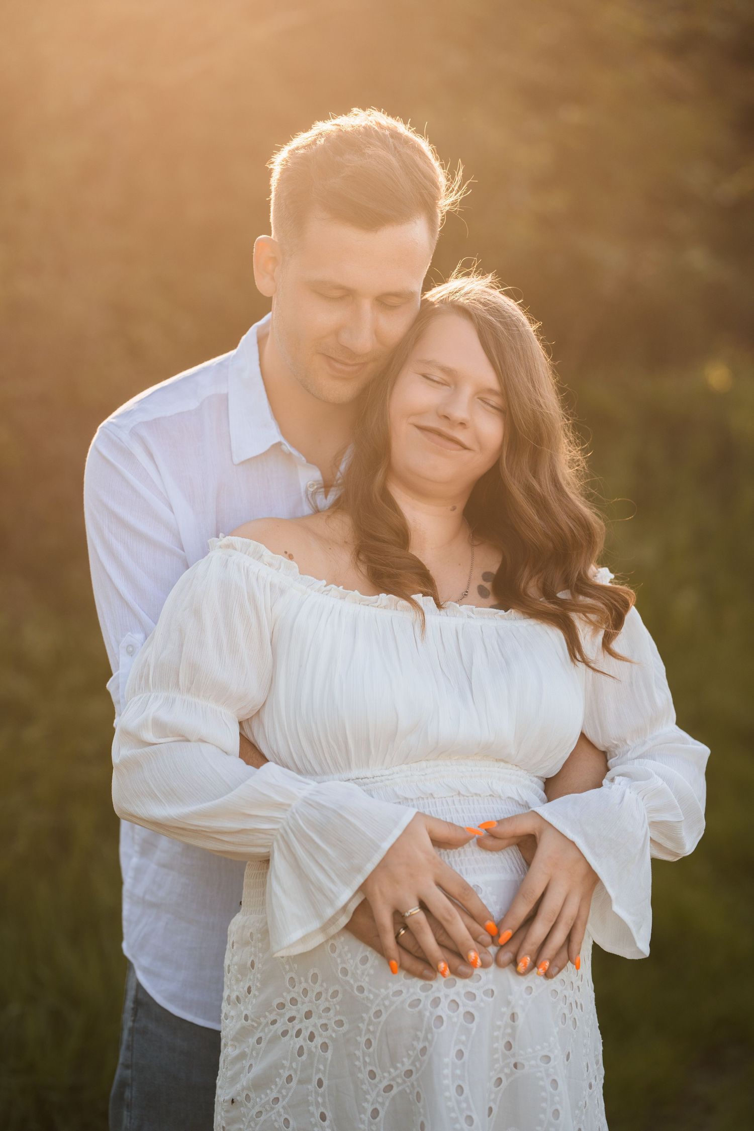 A romantic couple embraces during golden hour sunset, wearing white clothing in an intimate outdoor photoshoot.